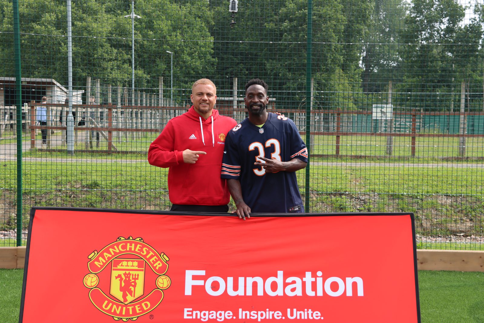 Wes Brown and Charles Tillman posing for a photo in front of the Manchester United Foundation sign